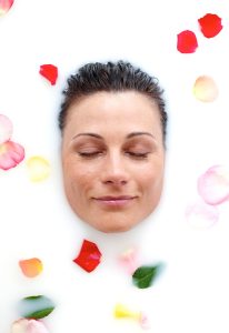 Das relaxte Gesicht einer Schönen umringt von Rosenblättern geniesst das Milchbad