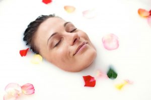 Das schöne Gesicht einer Frau lugt aus einem mit Rosenblätter umgebenen Milchbad