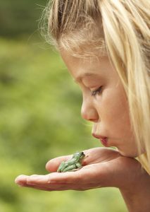 Junges Mädchen küsst den grünen Laubfrosch auf ihrer Hand