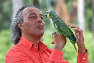 Mann in rotem Hemd kommuniziert liebevoll mit einem grünen Papagei