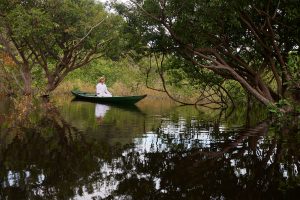 Foto einer stillen Nebenflusslandschaft des Rio Negro mit einem im Holzboot sitzenden meditierenden Mannes