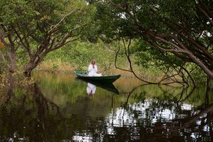 Foto einer stillen Nebenflusslandschaft des Rio Negro mit einem im Holzboot sitzenden meditierenden Mannes in Weiß