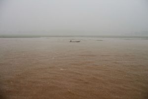 Foto zeigt die braune Flusslandschaft mit Boot des Rio Negro bei schwerem Regenschauer