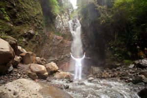Fotografie eines Mannes in weißer Kleidung vor einem Wasserfall segnend