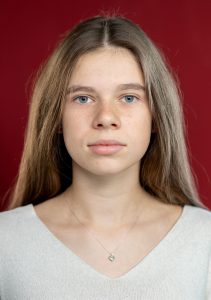 Portrait einer jungen Frau mit blauen Augen, langem Haar vor roter Wand