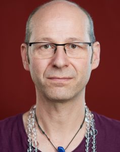Portrait eine Mann mit Brille vor rotem Hintergrund