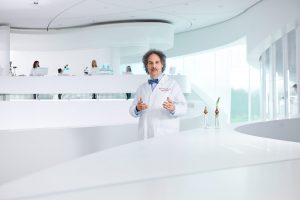 Portrait von einem Forschungsprofessor in eine großen, hellen Labor mit Mitarbeitern im Hintergrund