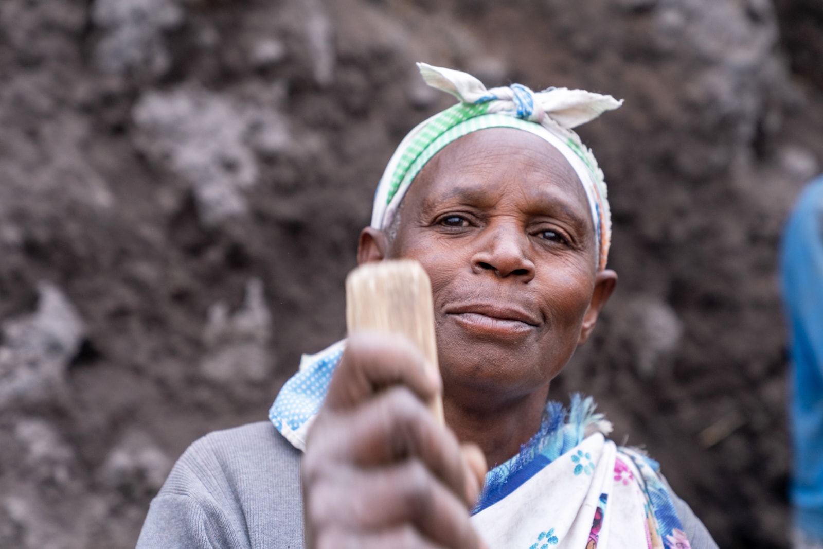 Portrait einer afrikanischen Frau mit geknotetem Kopftuch und geschultertem Schlaghammer im Steinbruch