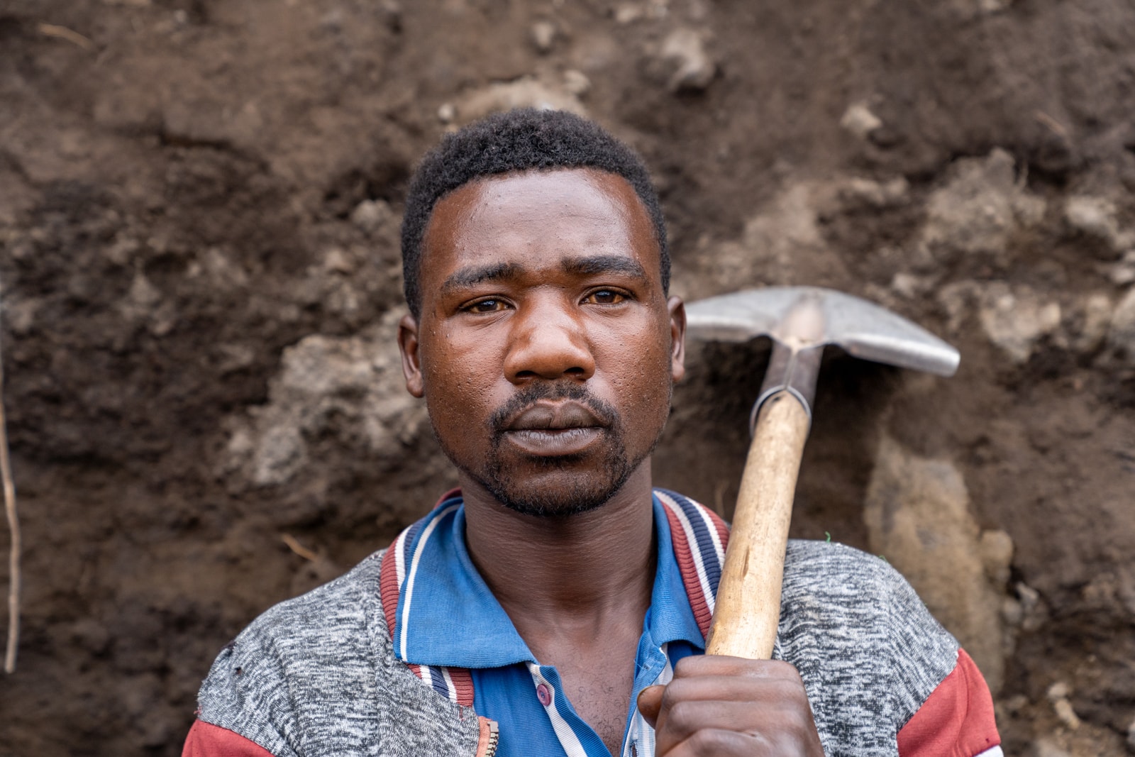 Portrait eines afrikanischen Jugendlichen und geschulterter Schippe im Steinbruch