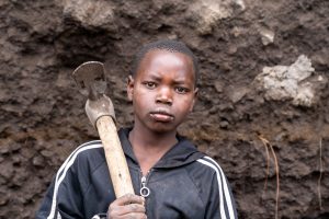 Portrait eines jungen afrikanischen Jungen und geschultertem Schlaghammer im Steinbruch