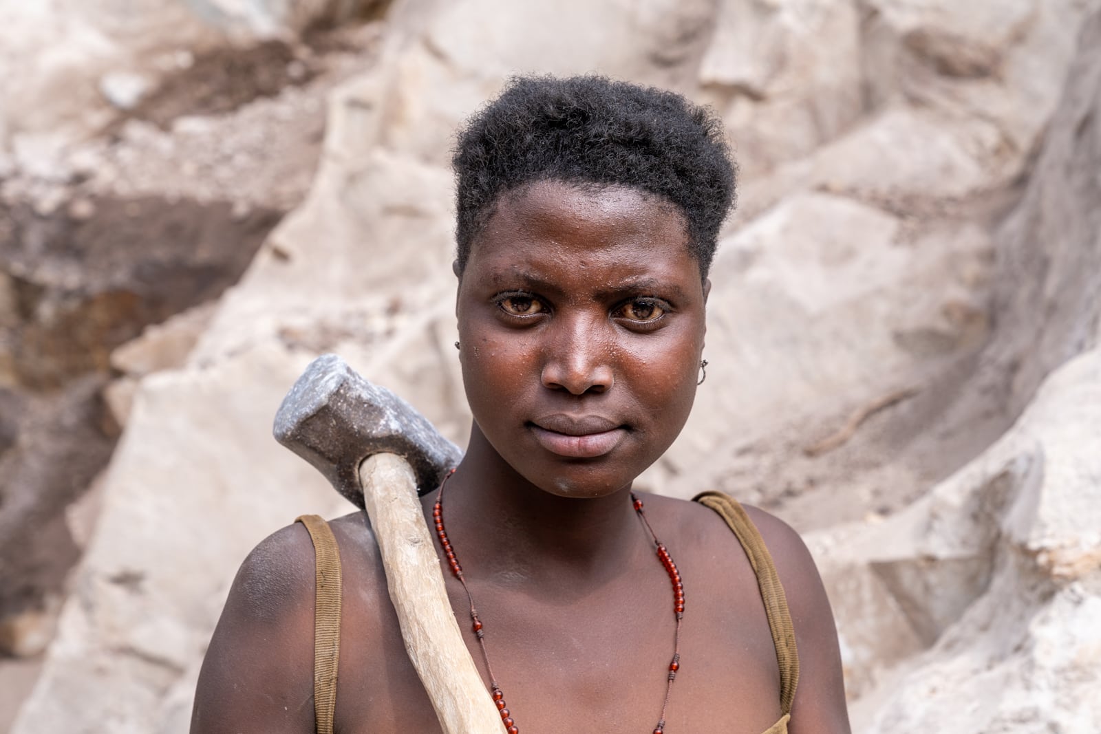 Portrait einer jungen afrikanischen Frau mit geschultertem Schlaghammer im Steinbruch