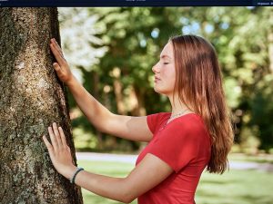 Foto einer jungen Frau in rotem Outfit einen Baum berührend